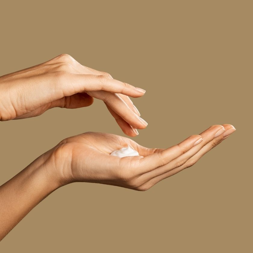 Two hands holding a small amount of cream against a beige background
