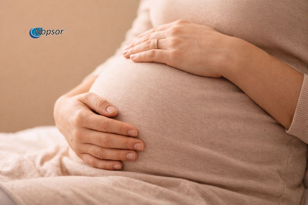 Close-up of a pregnant belly with hands gently touching it, against a beige background.