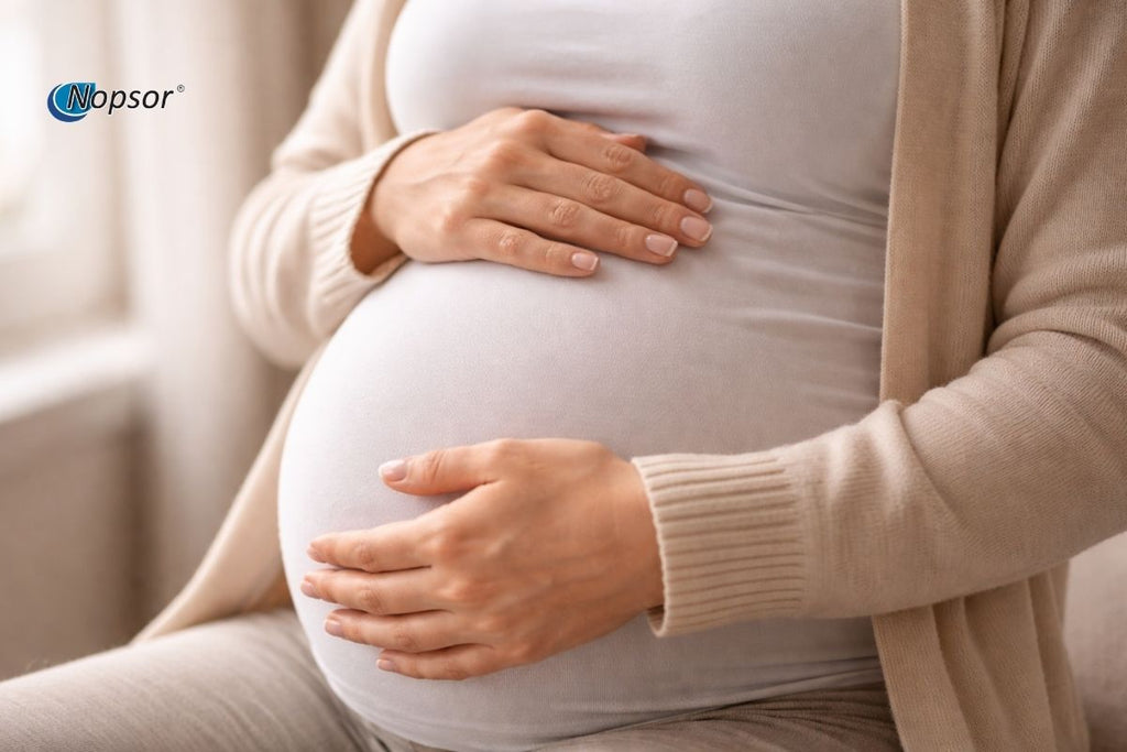 Pregnant person wearing a beige cardigan and holding their pregnant belly.